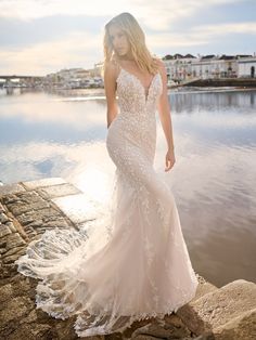 a woman in a wedding dress standing on the edge of a body of water at sunset