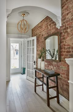 a room with a brick wall and wooden flooring next to a white door that has a mirror on it