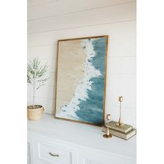 a painting hanging on the wall next to a white dresser with a potted plant