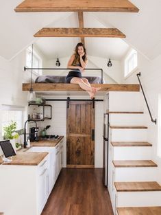 a woman sitting on top of a bed in a loft above a kitchen and stairs