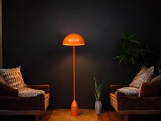 an orange floor lamp sitting next to two chairs in a living room with black walls