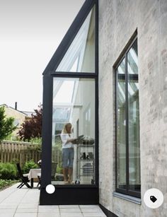 a woman standing in the doorway of a house with an open patio area and large windows