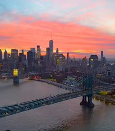 an aerial view of the city and bridge at sunset, with skyscrapers in the background