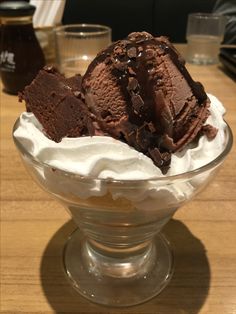 two scoops of ice cream sit in a glass bowl on a wooden table top