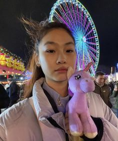 a woman holding a pink stuffed animal in front of a ferris wheel