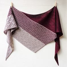 a knitted scarf hanging on a clothesline next to a white wall and wooden pegs