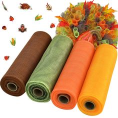 three rolls of orange, green and brown fabric next to an autumn tree with leaves on it