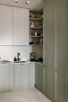 a kitchen with white cabinets and marble counter tops, along with open shelving above the sink