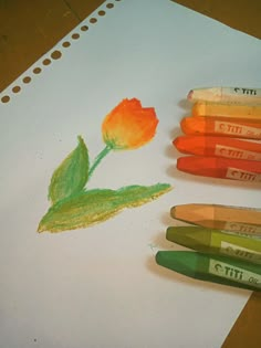 some crayons are laying on top of a piece of paper with a flower