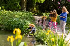 three women and two children are fishing in the water near some yellow daffodils