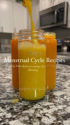 three jars filled with orange and yellow liquid on top of a marble countertop next to an oven