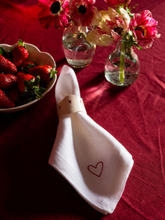 two vases filled with flowers and strawberries on top of a red table cloth