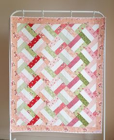 a pink and green quilt is hanging on a white rack in front of a wall