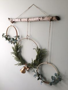 two circular wreaths hanging on a wall with metal bells and greenery around them