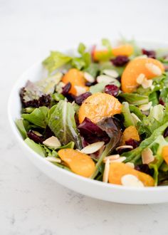 a salad with oranges and almonds in a white bowl