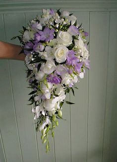 a bouquet of white and purple flowers hangs from the wall in front of a person's hand