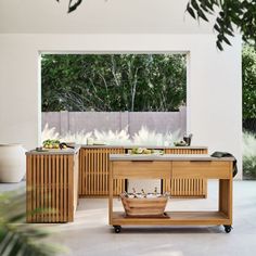 an outdoor kitchen with wooden furniture and plants on the counter top, in front of a large window