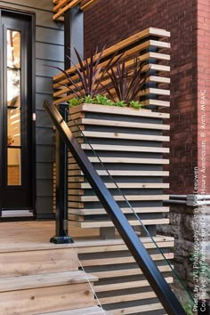 a wooden stair case with plants in it on the side of a brick building next to a black door