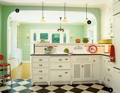 a kitchen with checkered flooring and white cabinetry has green walls, an arched window, and two red chairs