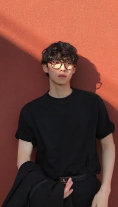 a young man wearing glasses leaning against a wall