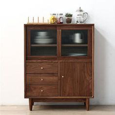 a wooden cabinet with glass doors on the top and bottom, in front of a white wall