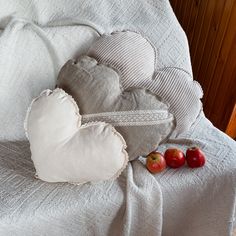 a heart shaped pillow sitting on top of a white bed next to two red apples