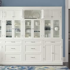 a large white cabinet with glass doors and drawers in a blue wall room next to a rug on the floor