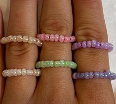 four different colored beads on the fingers of someone's hand and one is wearing a ring