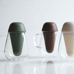 three glass mugs with lids and handles are lined up in a row on a white surface