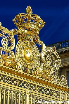 an ornate gold clock on top of a golden fence with blue sky in the background