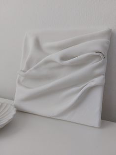 a close up of a white pillow on a table with plates and a bowl in the background