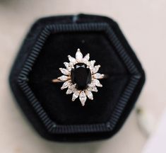 an engagement ring with a black diamond surrounded by white diamonds in a velvet box on top of a table