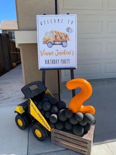 a birthday party sign with balloons in the shape of a dump truck and an orange number 2