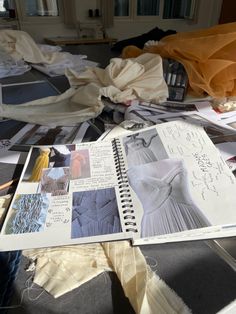 an open book with pictures and clothes on it sitting on top of a table covered in papers