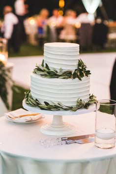 a wedding cake sitting on top of a white table next to a glass of water