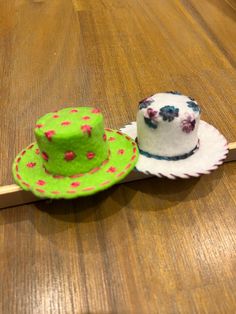 two small hats sitting on top of a wooden table next to each other, one green and the other white