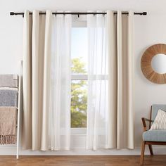 a living room with white curtains and a round mirror on the wall next to a chair