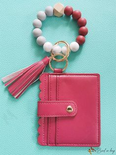 a pink wallet with tassels and a beaded bracelet on it sitting on a blue surface