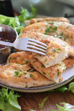 a plate filled with chicken and sauce on top of lettuce next to a fork