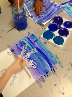 a child is painting with watercolors on paper and another kid is holding a brush