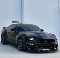 a black sports car parked in front of a garage door with its hood up and lights on