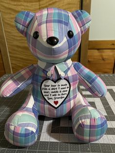 a blue and pink teddy bear sitting on top of a checkered tablecloth covered floor