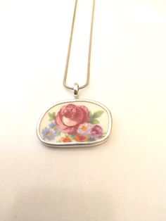 a necklace with a pink rose on it sitting on a white table next to a silver chain