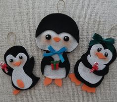 three felt penguin ornaments are hanging on the wall, one is holding a christmas present