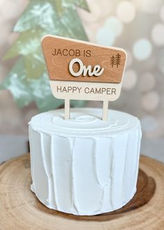 a white cake with a wooden one sign on it's top that says, jacob is one happy camper