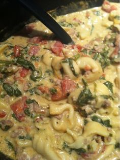 a pan filled with pasta and spinach covered in cheese, sauce and meats