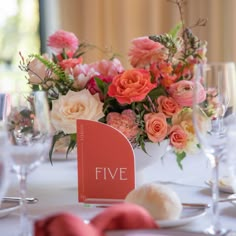 the table is set with pink and orange flowers in vases, napkins, and wine glasses