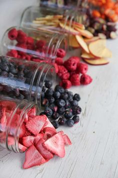 several jars filled with different types of fruit on a white wooden table, including raspberries, blueberries, and peaches