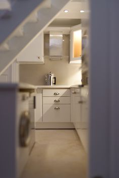 a kitchen with white cabinets and drawers under a stair case that leads up to the second floor