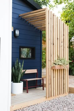 a small blue house with a wooden pergolan on the side and a bench in front